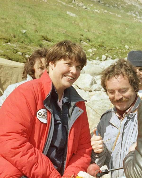 a woman in a red jacket smiling and speaking to other people nearby