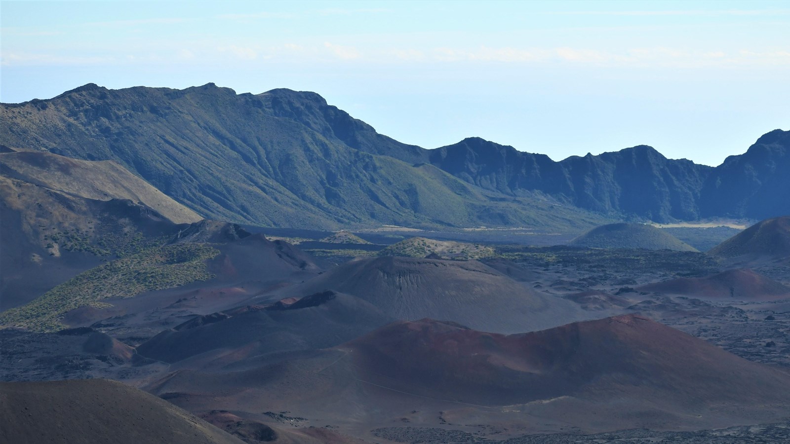 several colorful hills of cinder and vegetation against blue sky
