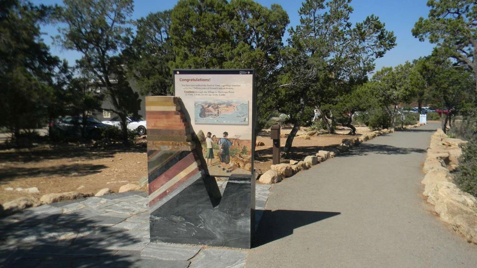 paved footpath with a stone entry monolith portal sign showing colorful stratified rock layers