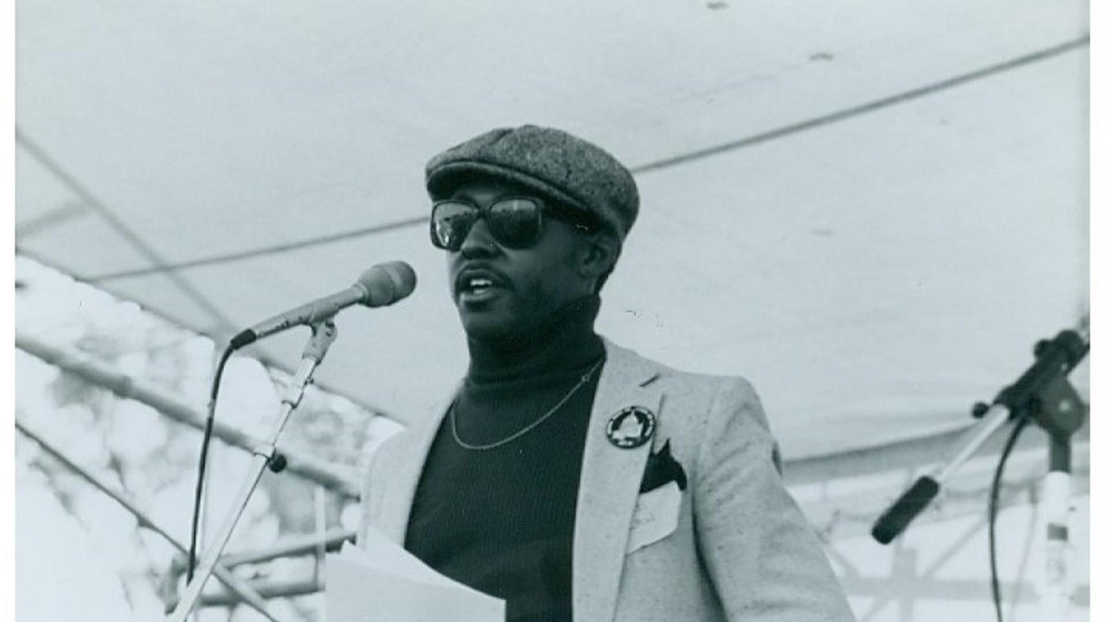 Man speaking into a microphone wearing a black button