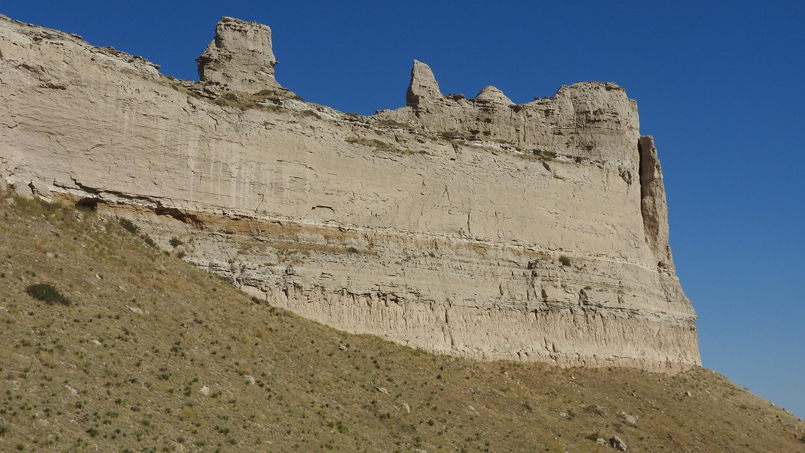 A large rock formation with visible strata and large chunks of rock at its base. 