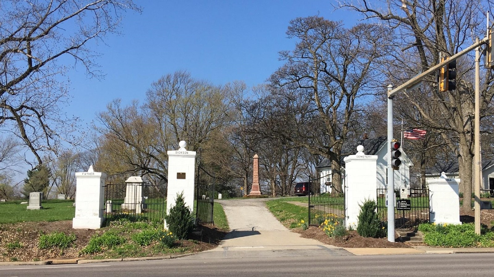 Four white marble columns leading to a cemetery with a paved walkway in the middle of the columns.