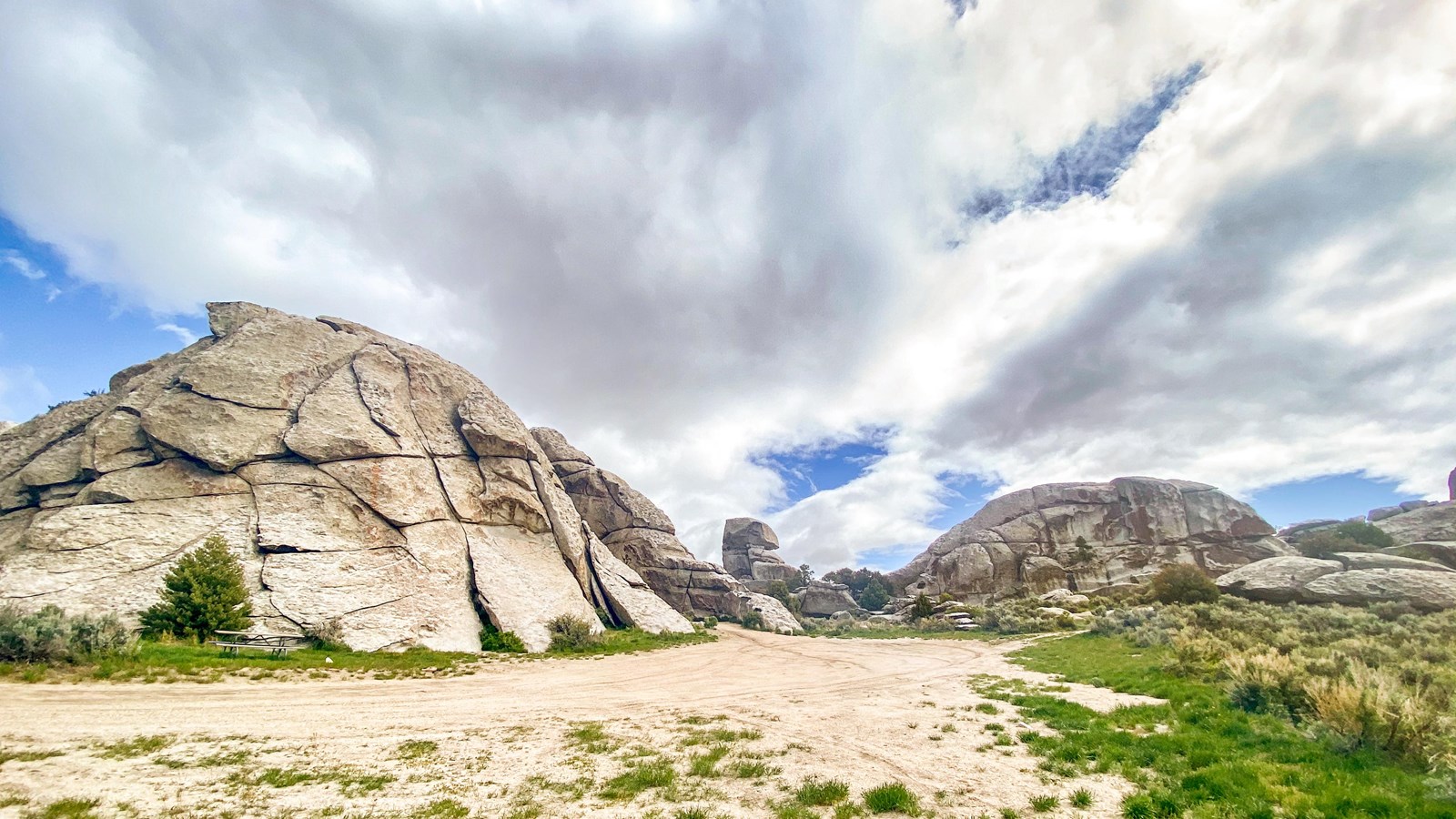 Large dome-like granite formations, gravel driveway green grass, and fluffy clouds.