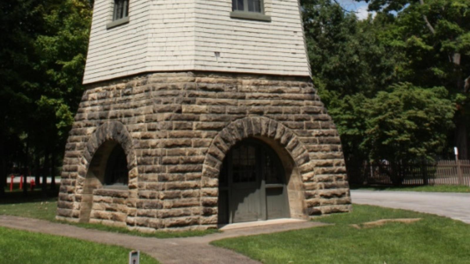 a tall windmill that has a stone base and white paneling with a weathervane on the top