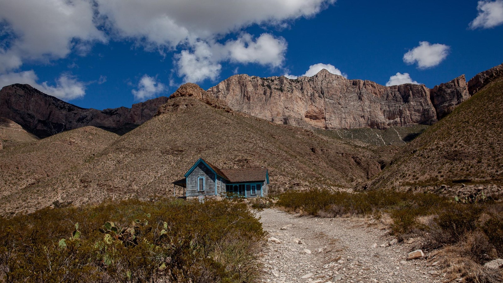 A wood frame home sits below tall limestone mountains