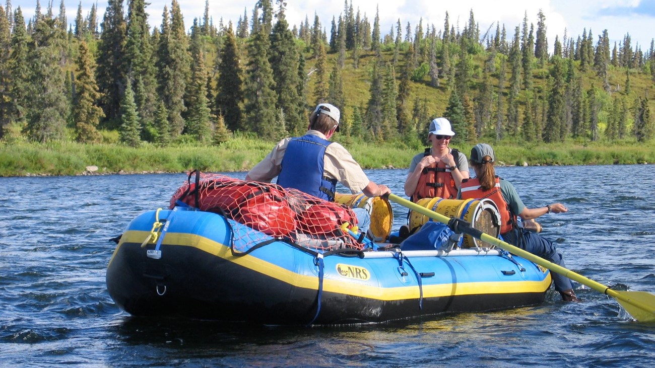 Three people in a raft on the water with trees in the background