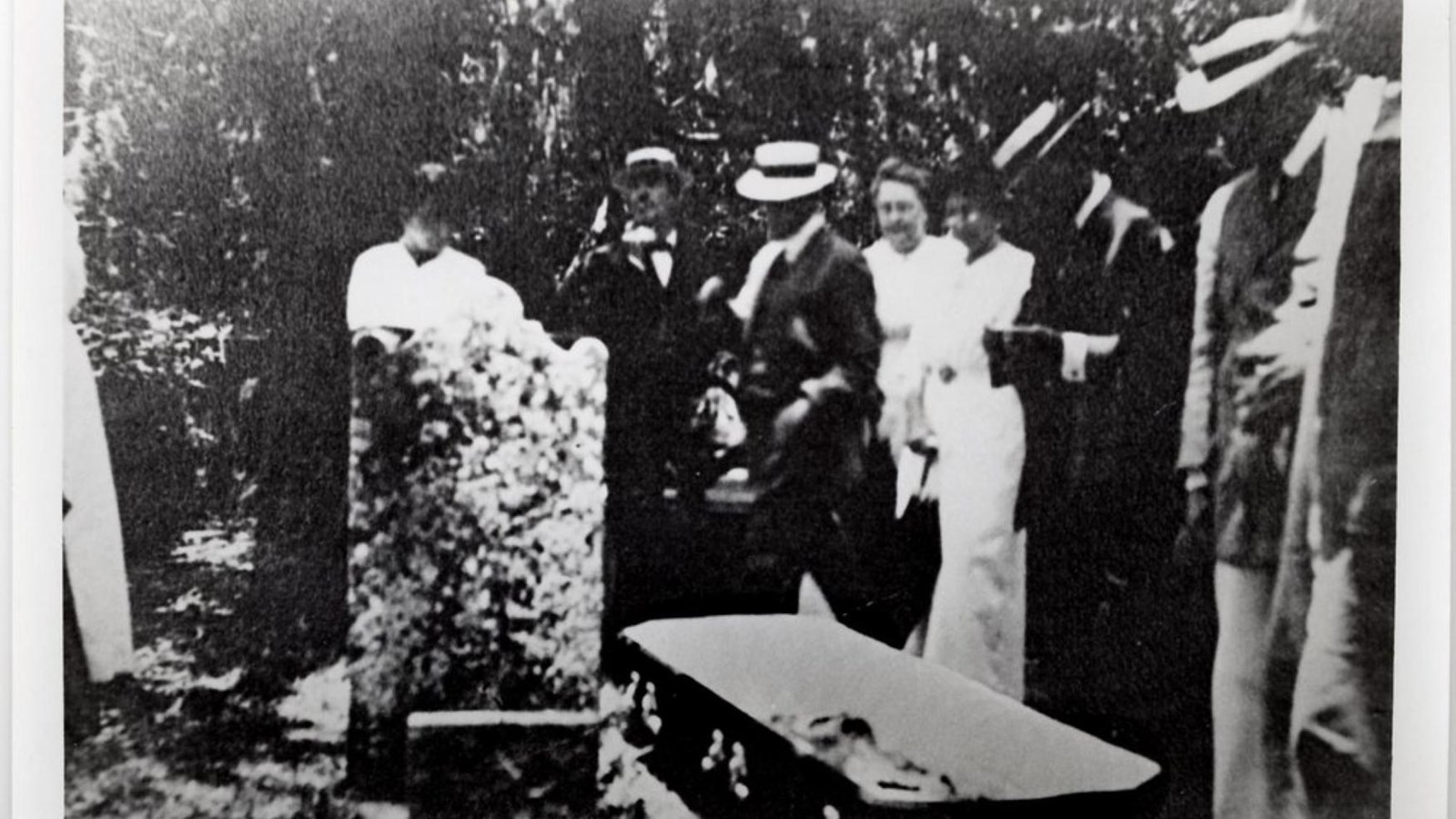Black and white photo of burial ceremony with persons surrounding a casket.