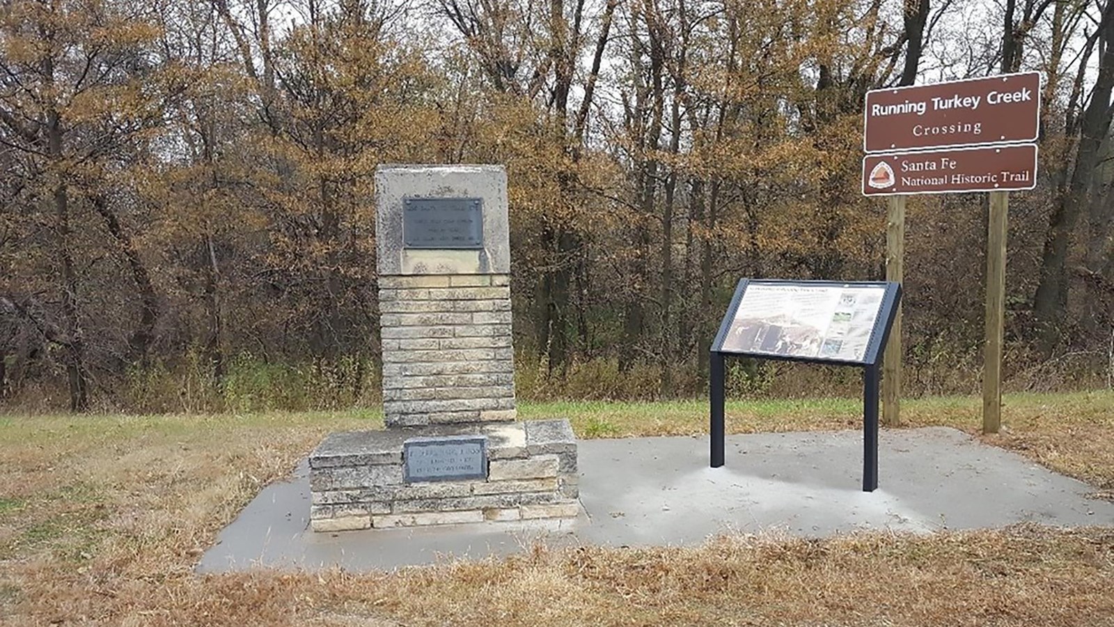 Wooded area with a stone marker, wayside sign, and Santa Fe National Historic Trail sign