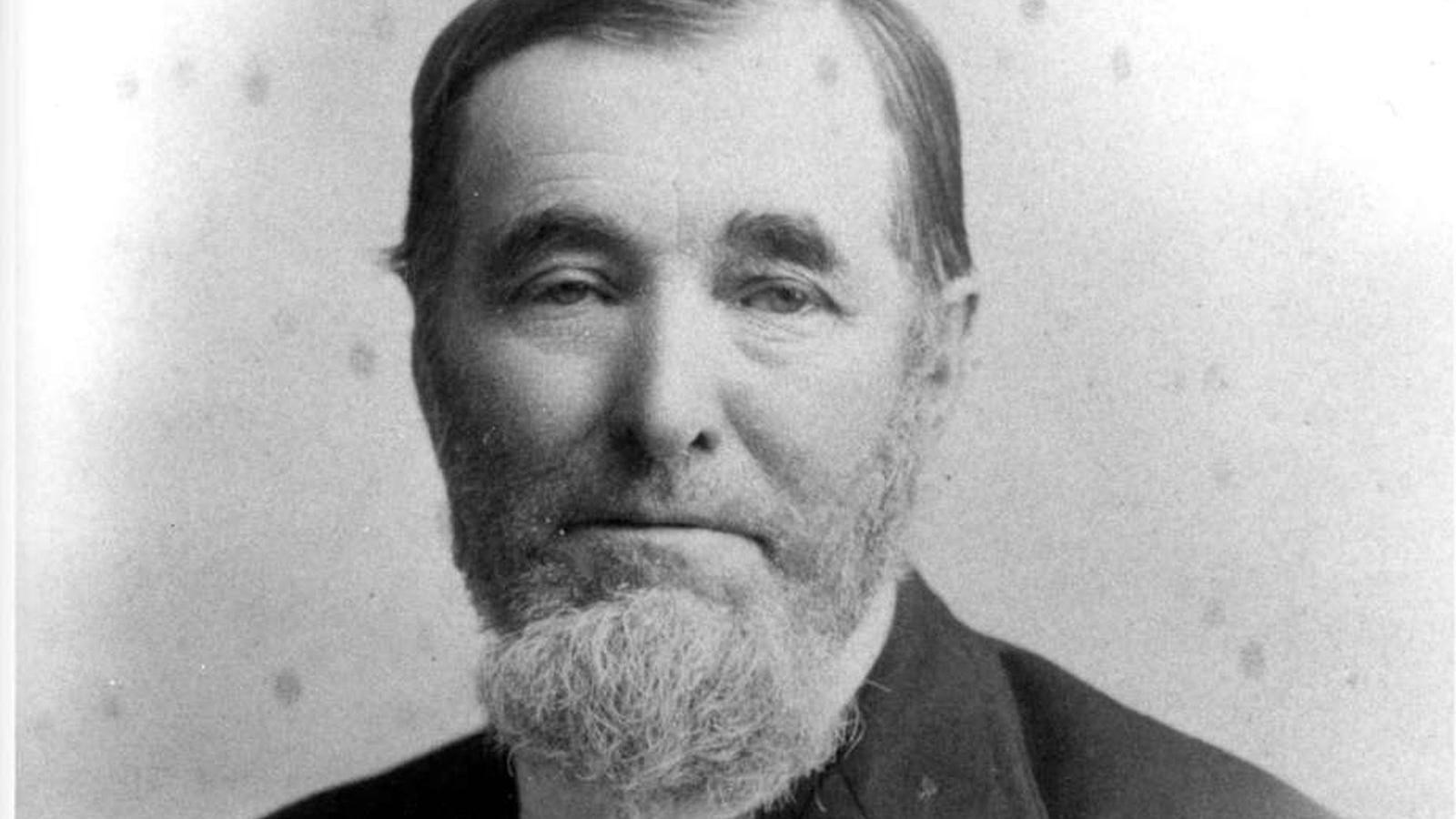 An 1880s photo depicts a man with a white beard showing little emotion.