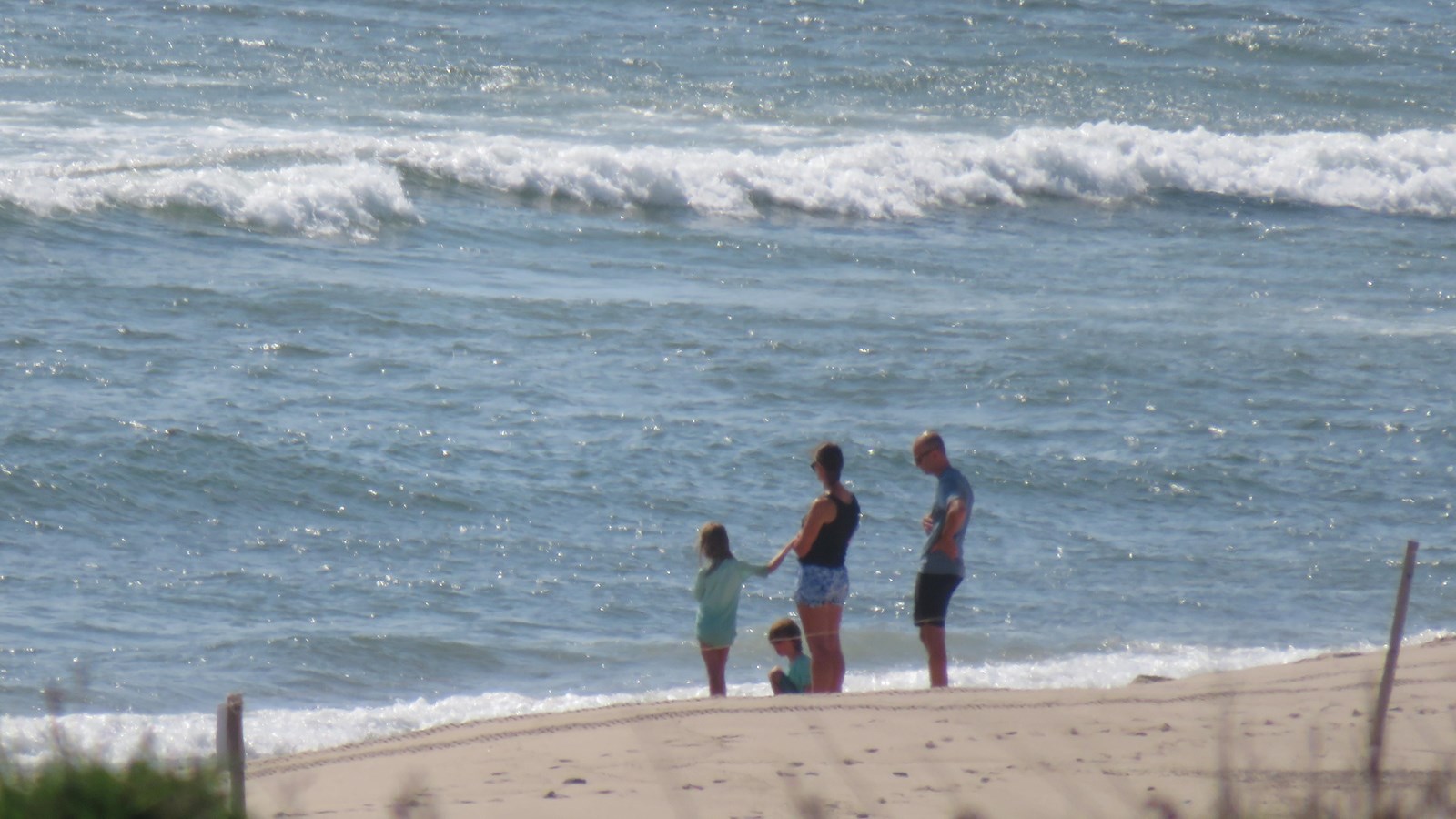 A man, woman, and two children stand together on the beach as the waves roll in.