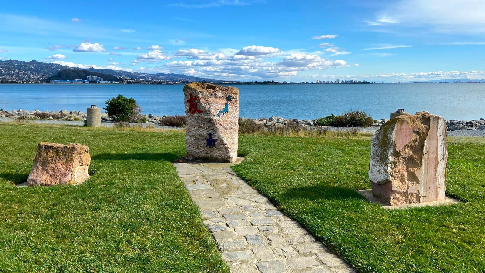 Three stones with Japanese characters seen on a grassy knoll by the bay.