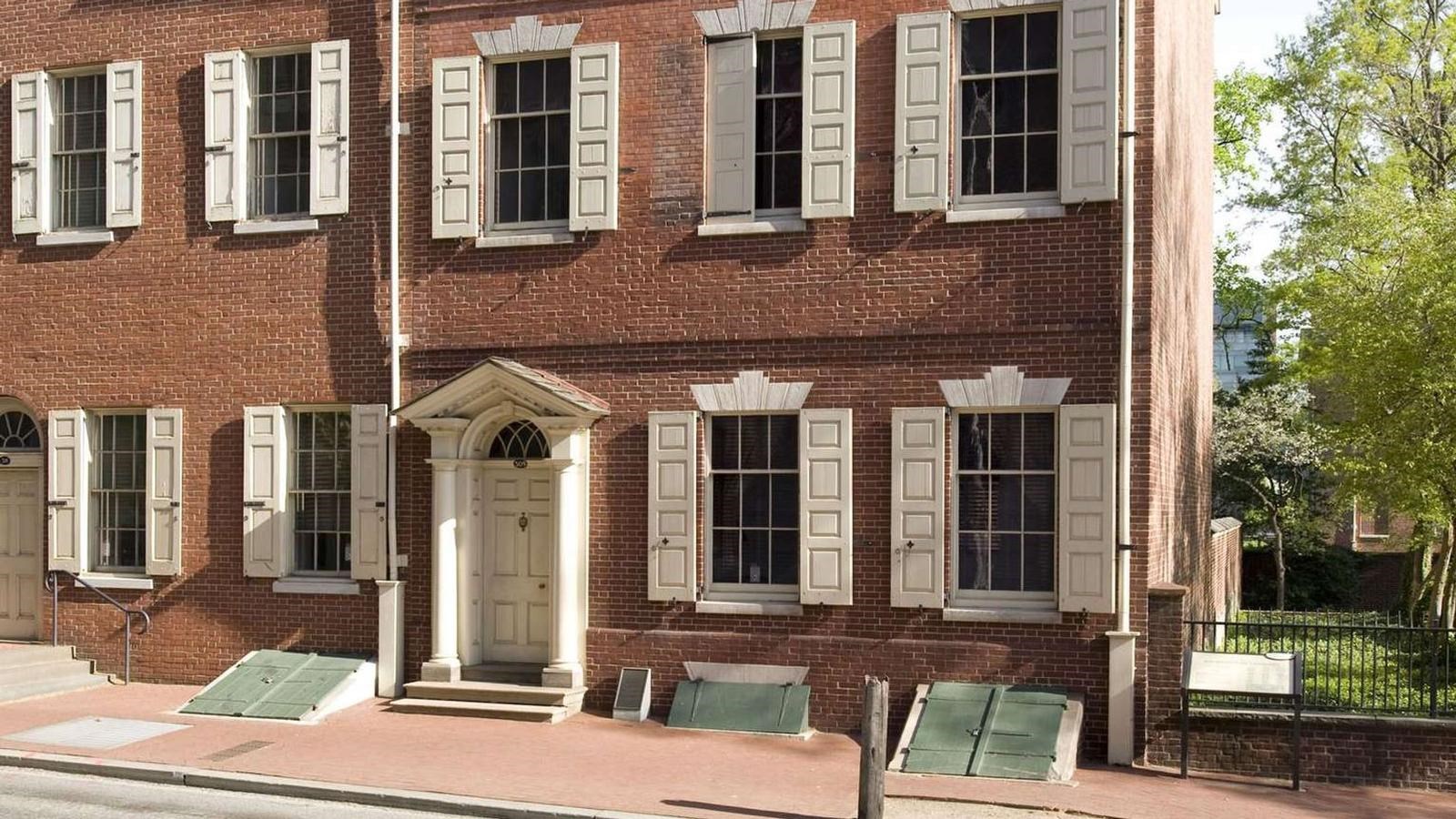 A color photo of a three-story red brick row house showing windows with white shutters.