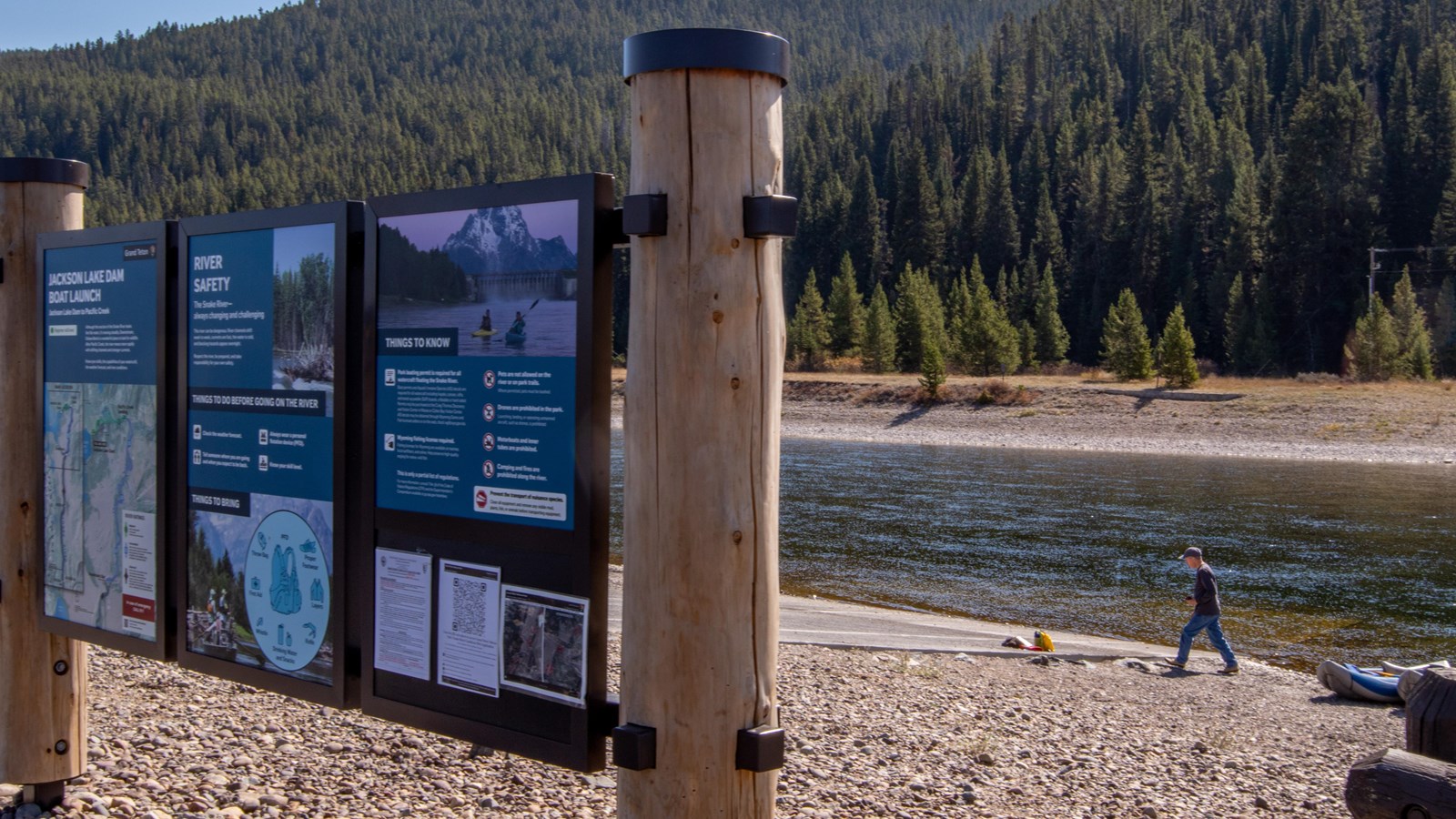 A large three panel sign displays information with a man and boat along a river in the background.