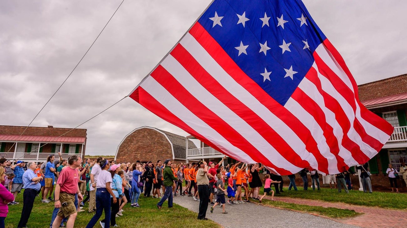 A group of visitors help raise a large garrison flag over Fort McHenry