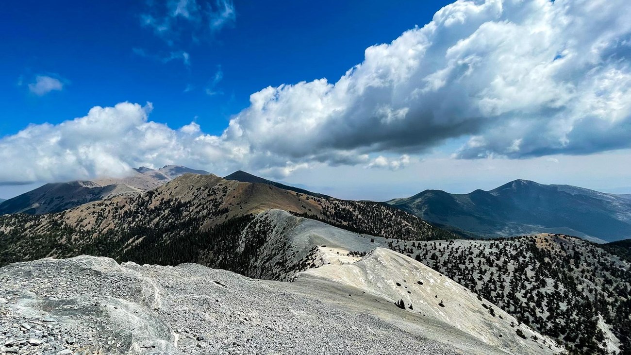 a bare alpine ridge with blue sky and white puffy clouds above.