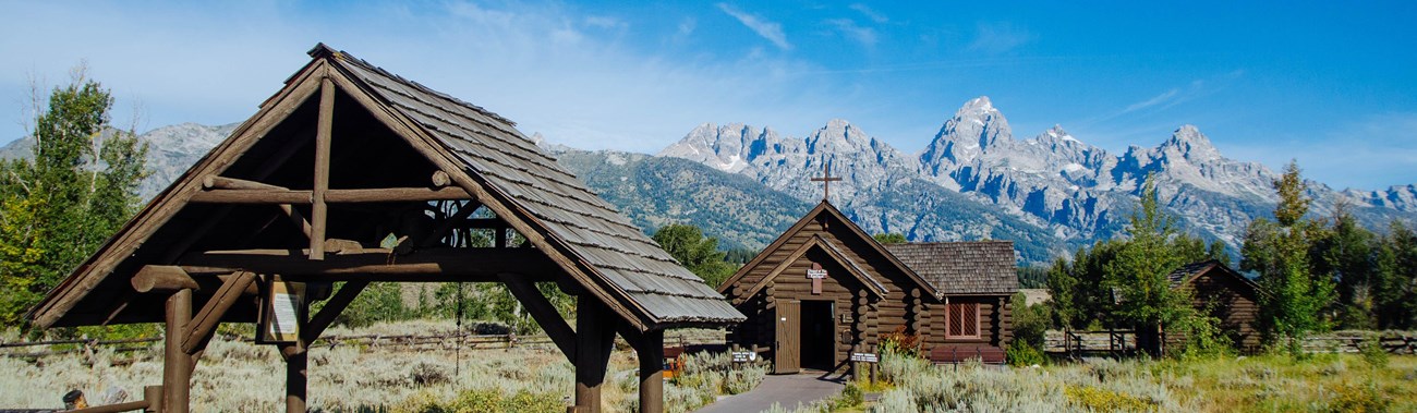 A log chapel in front of mountains.