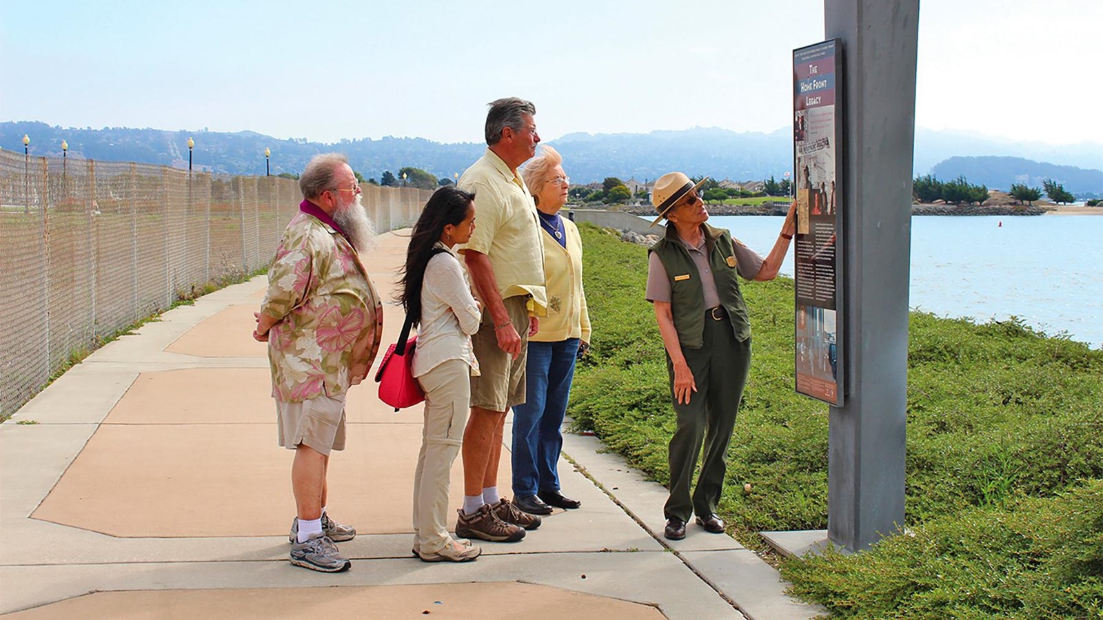 A female ranger, two other women and two men view a wayside marker on the Bay Trail.