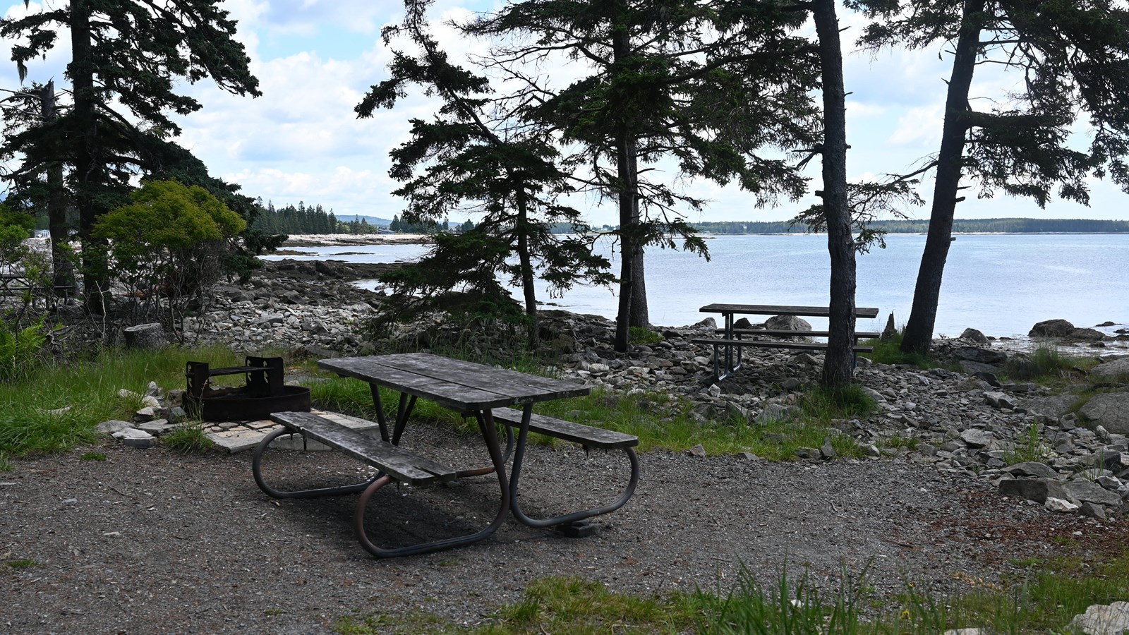 A small flat area surrounded by rocks and trees and the ocean with a picnic table