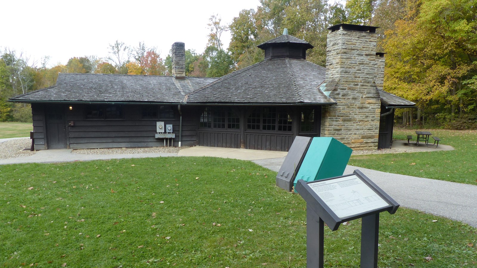 Brown wooden building with 3 stone chimneys and an octagonal main section lined with small windows.