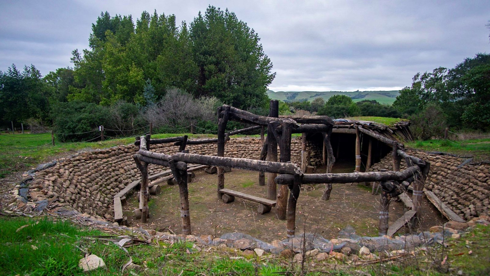 A round depression in the ground lined with rocks. 12 poles surround 4 poles around a center pole.