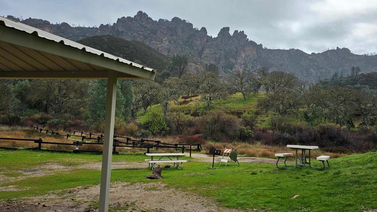 Shade structure and two picnic tables set before rock formations peering out of fog in winter