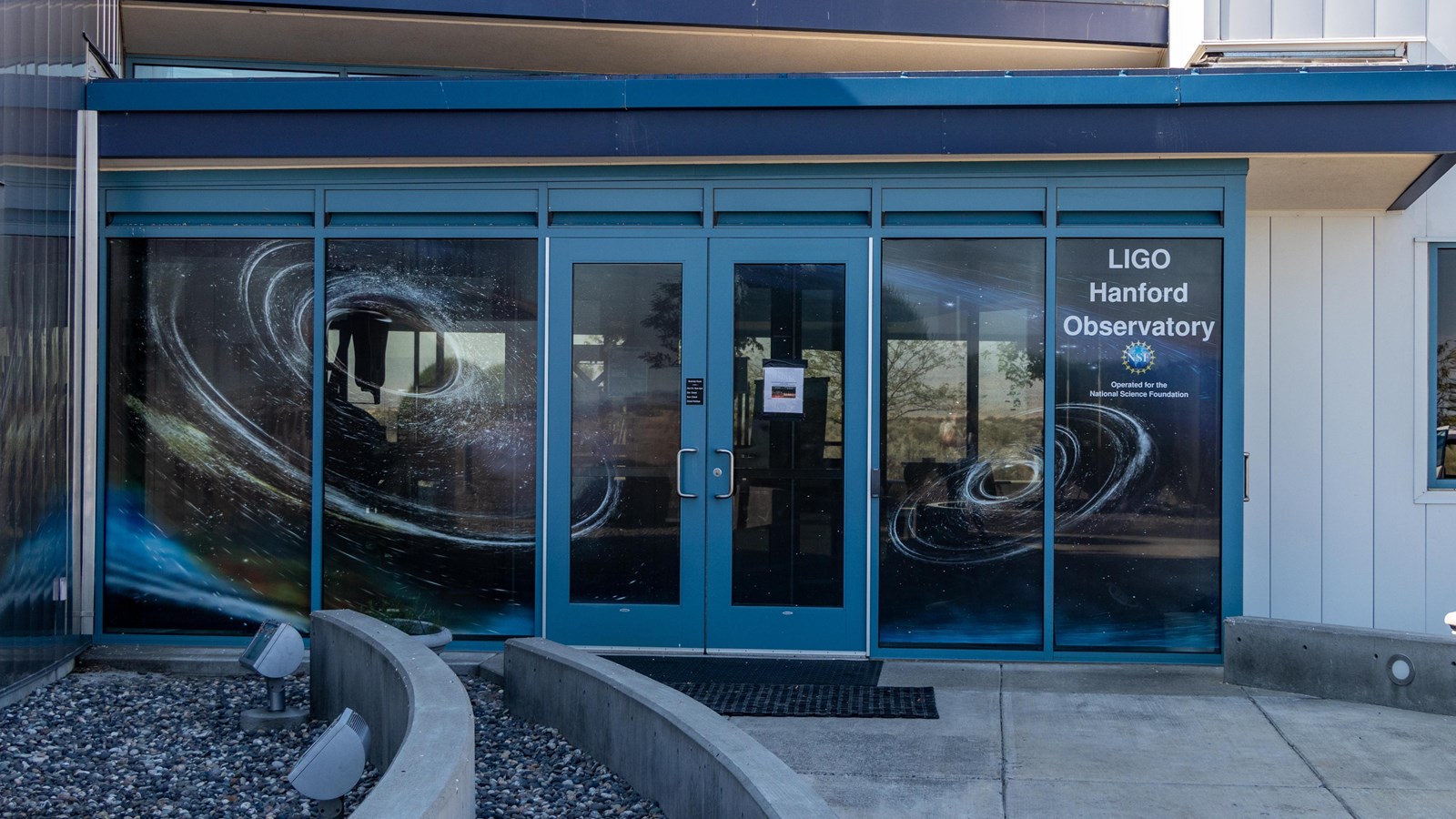 Color photograph of three windows with blue frames surrounding two glass doors with blue frames.