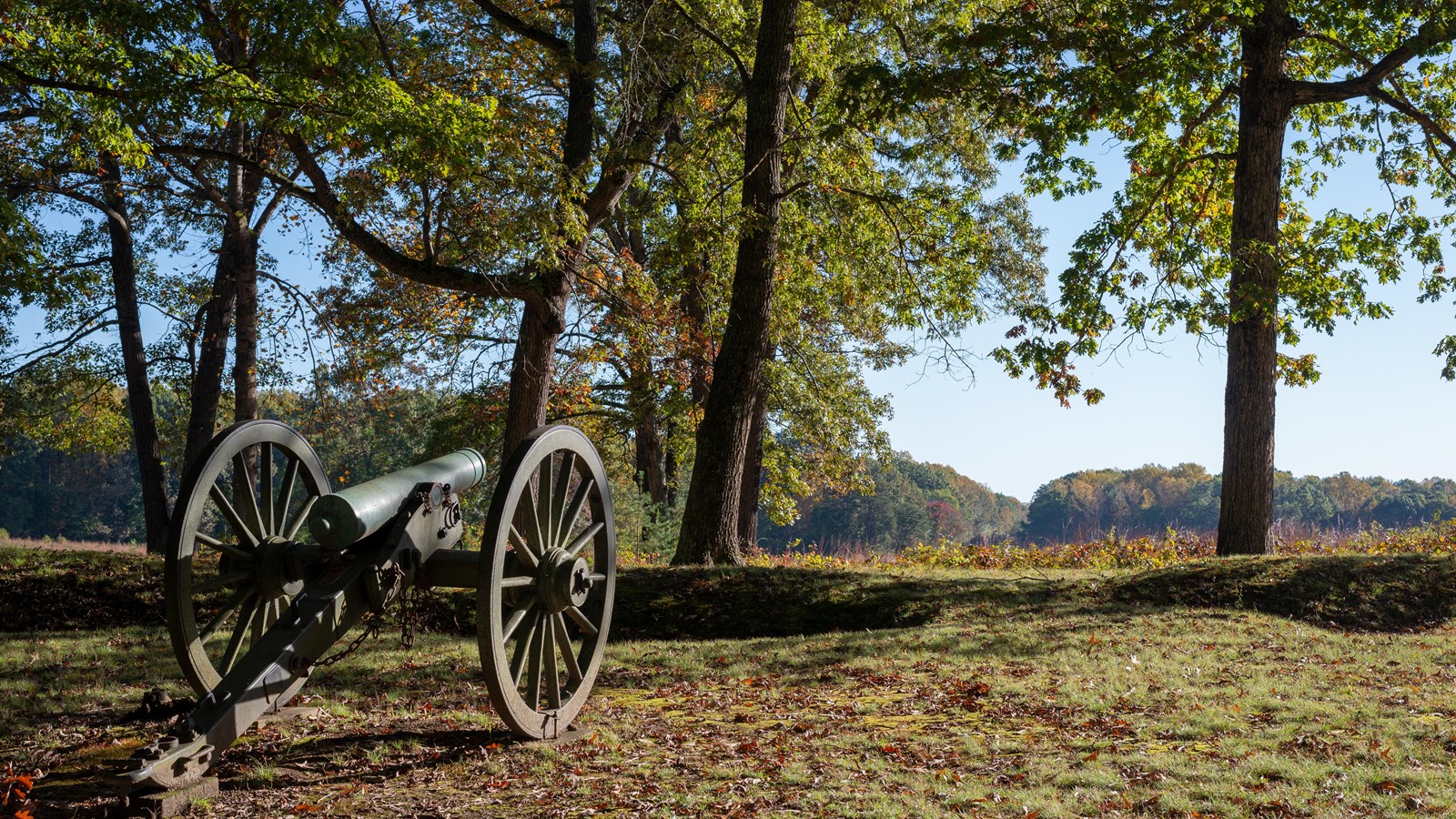 A cannon perched on a knoll overlooking a wide open field.