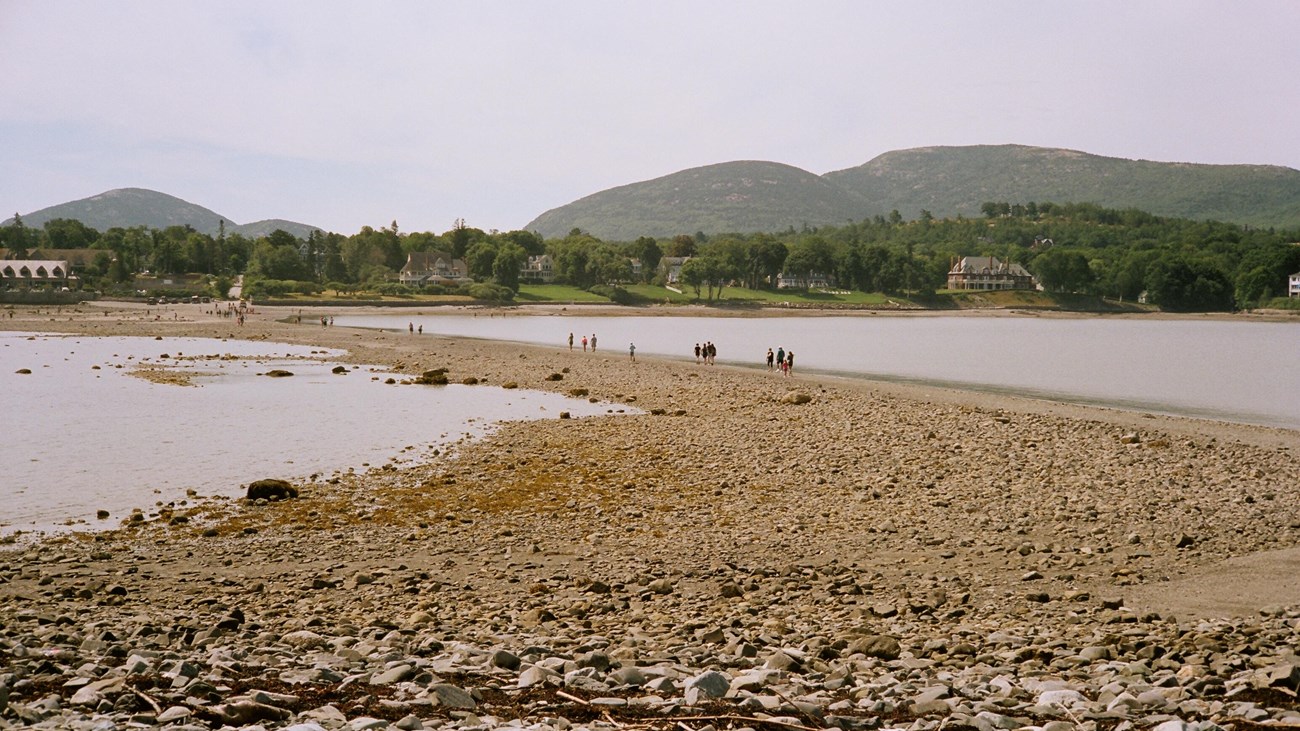 People walking across an exposed sand bar between an island and the mainland