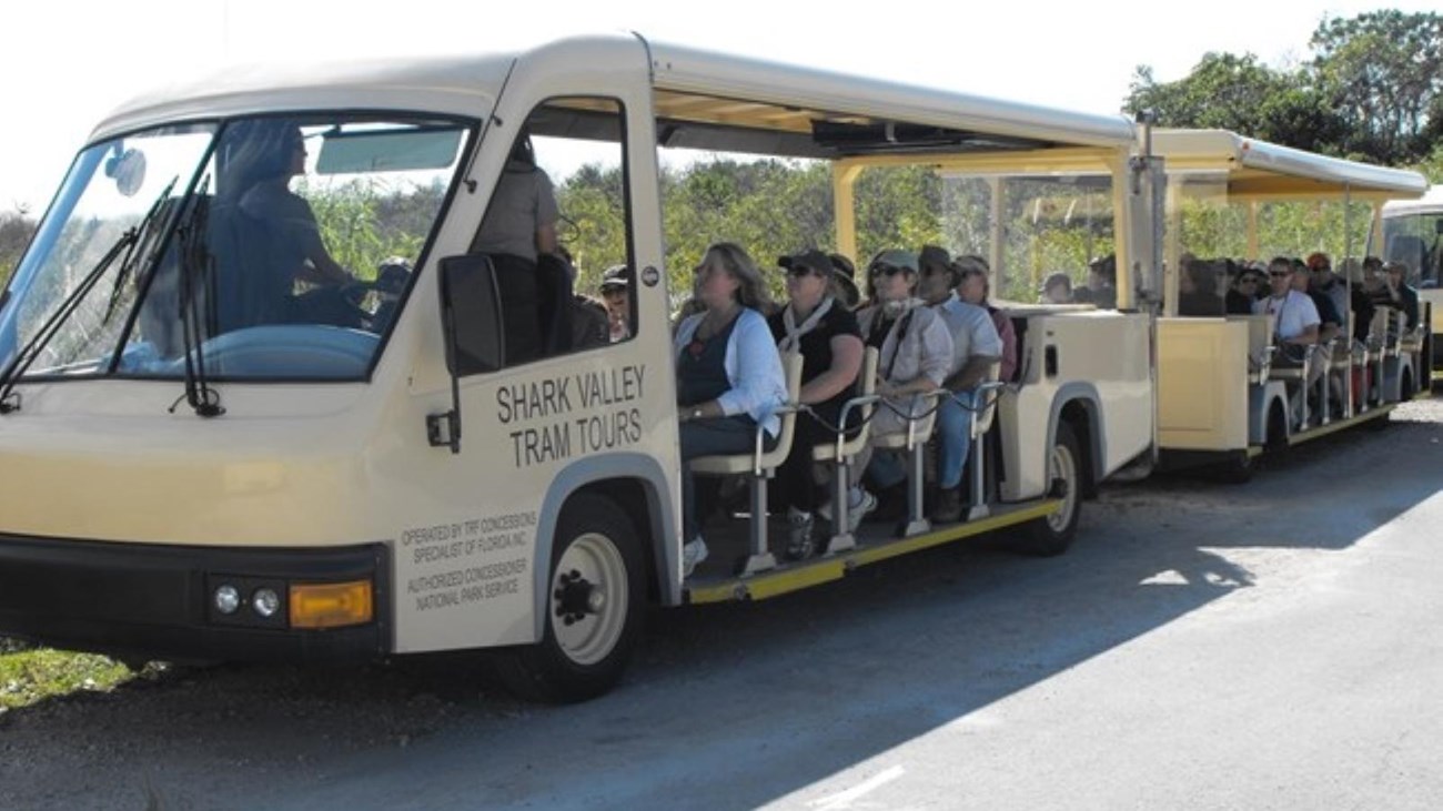 Passengers sit in a beige open air tram. A ranger sits facing the audience.