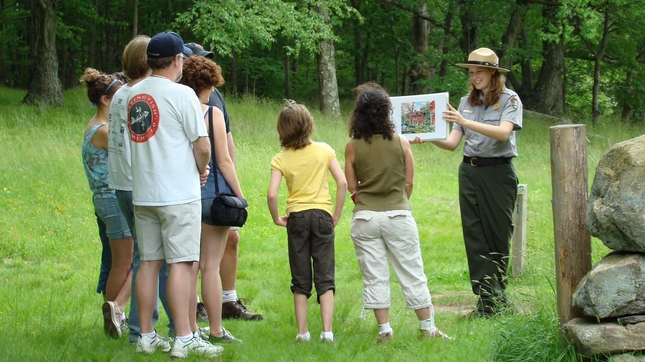 A ranger holding up an image with a group of visitors looking on.