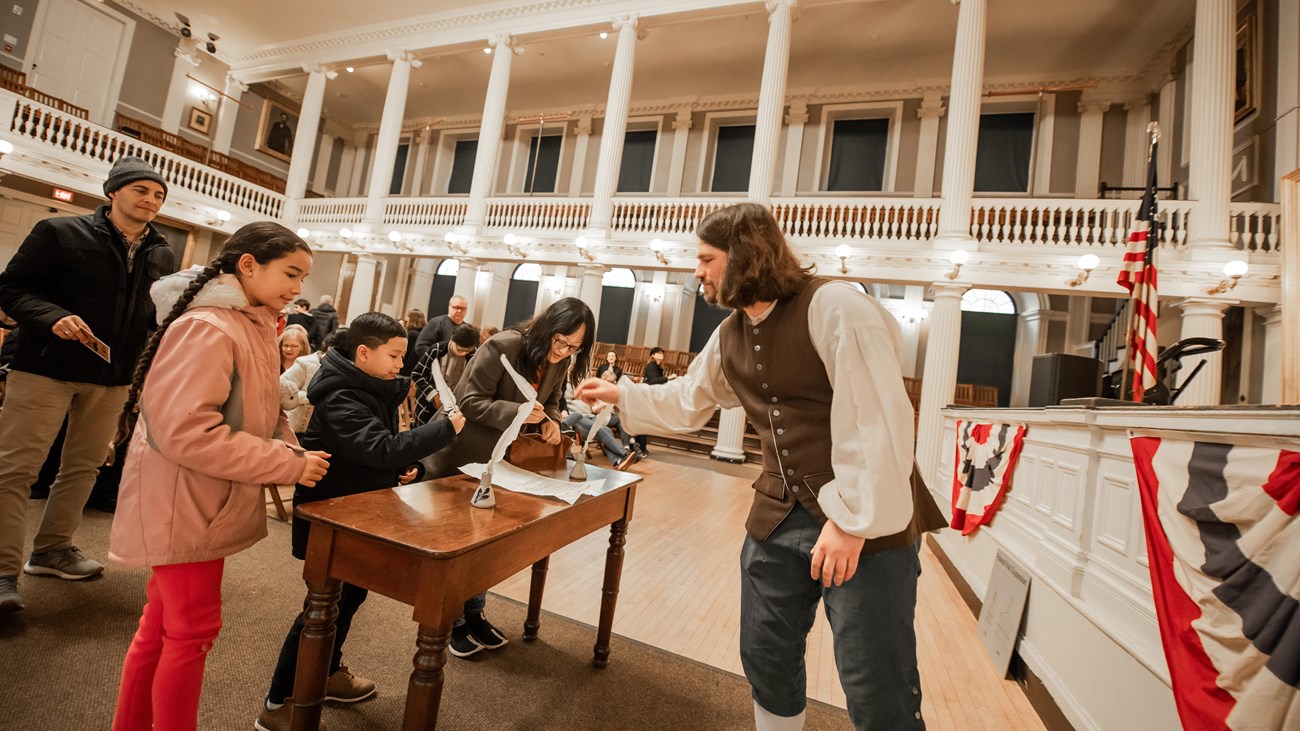 A Park Ranger in 1800s dress smiles as a kid signs the resolutions