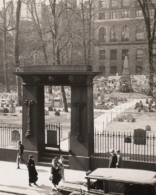 Historical photo of a burying ground with an granite gate and headstones in the background.