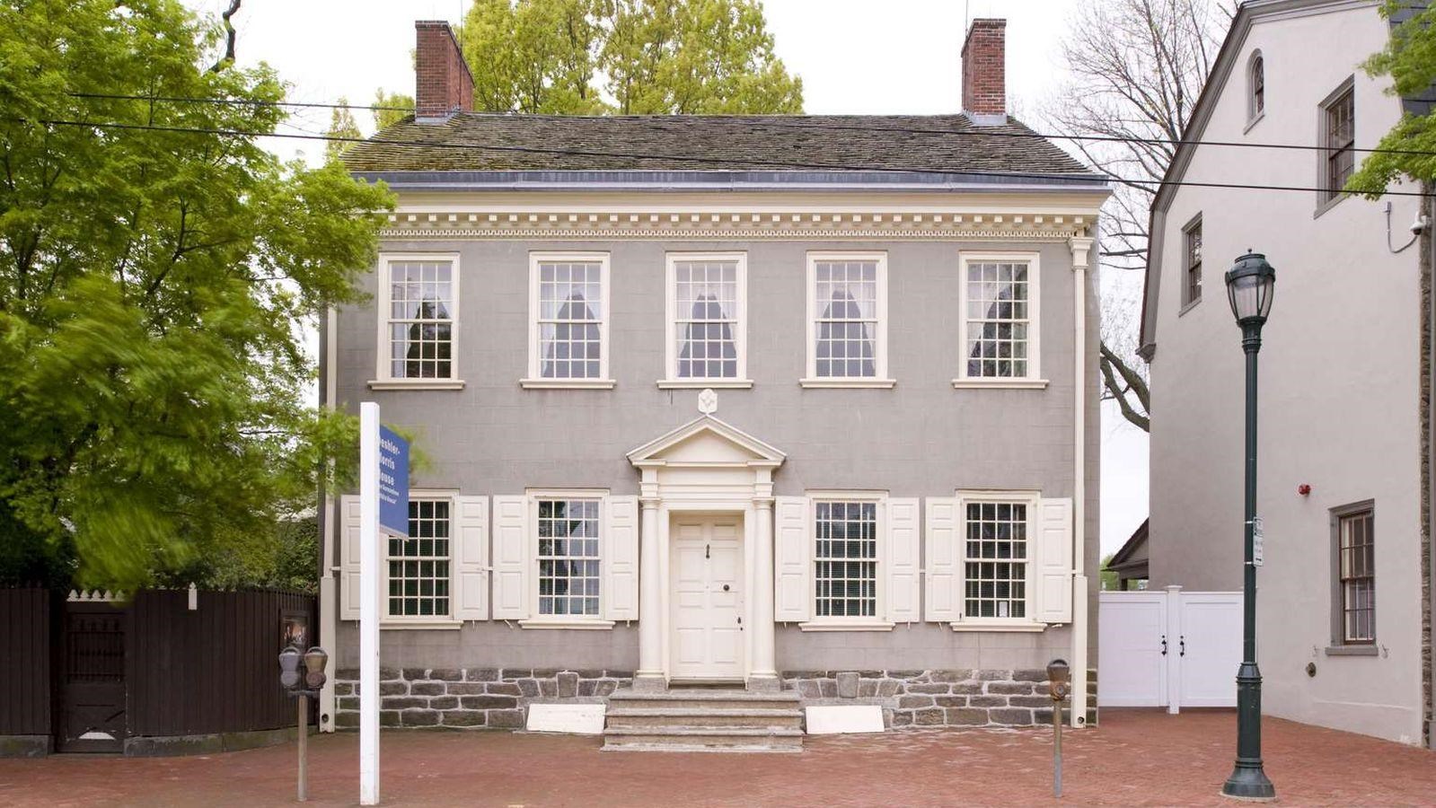 A color photo showing the exterior of a two story home with a central doorway and two end chimneys.