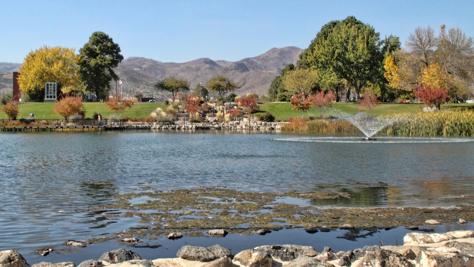 With mountains and fall foliage in the background, a fountain sprays water out of a small pond.