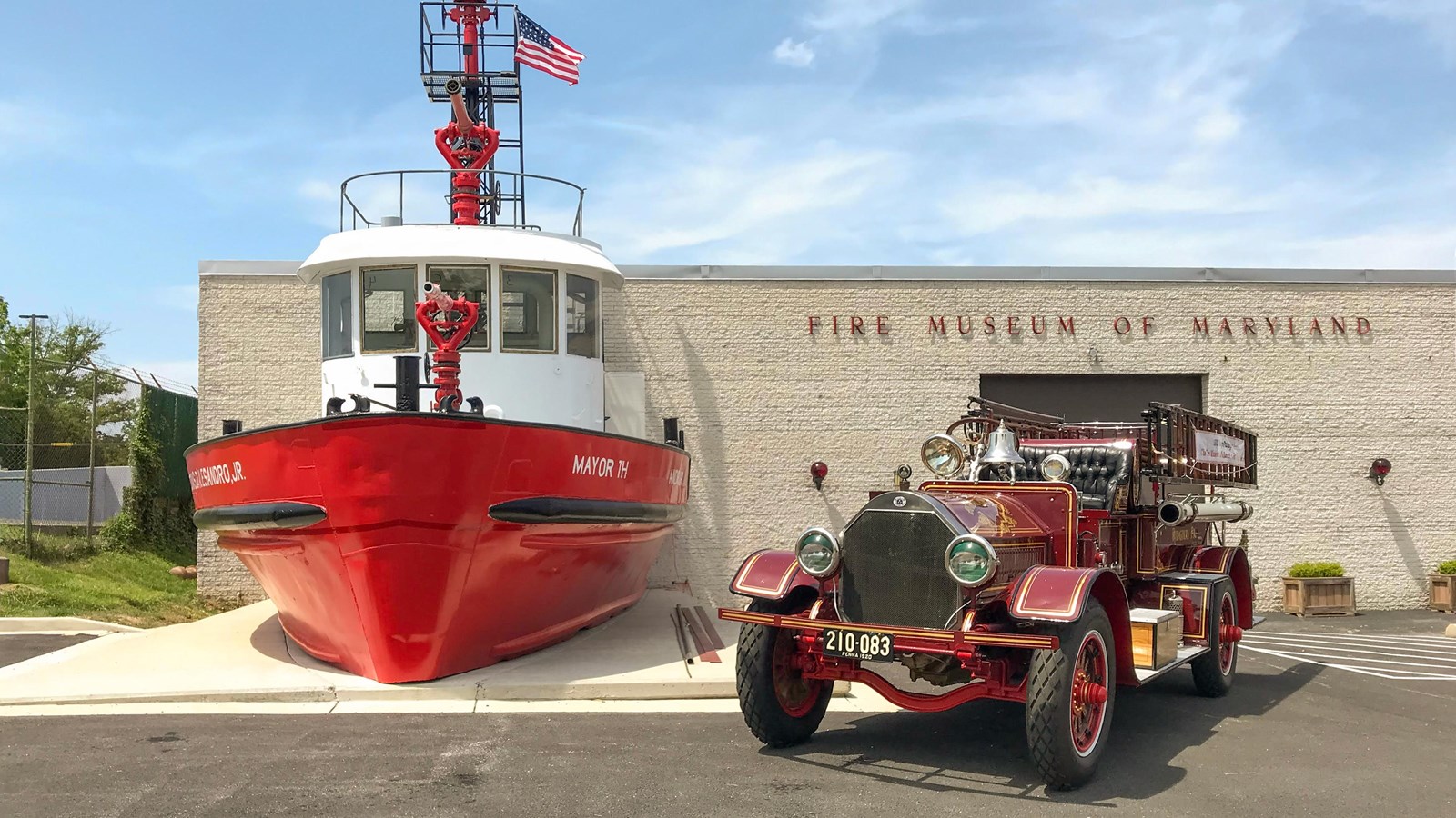 A red fireboat and an antique fire engine are displayed outside the Fire Museum of Maryland.