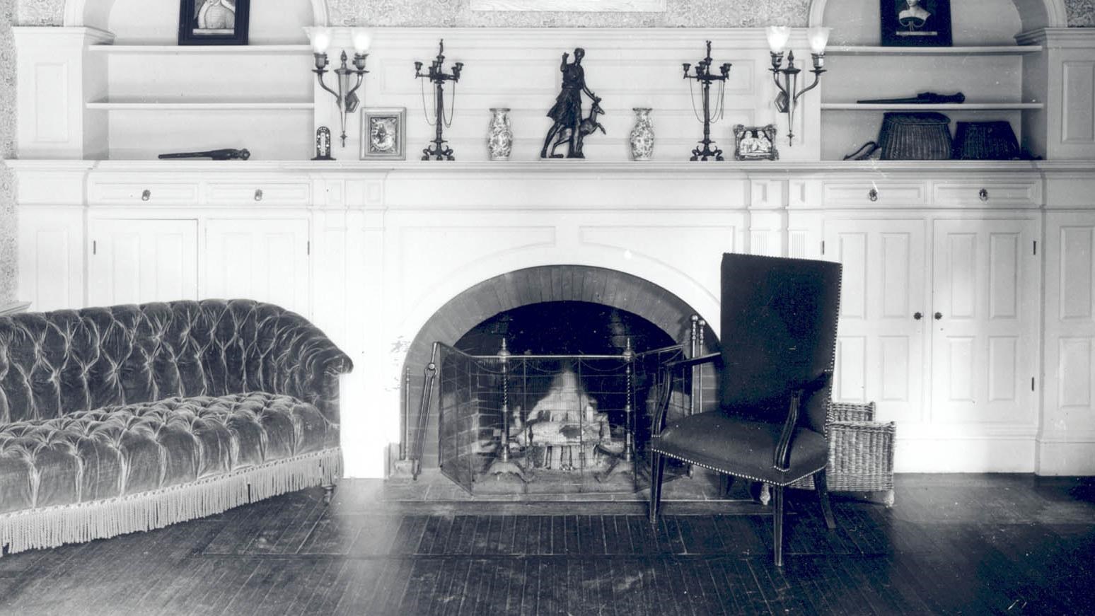 Interior of a historic home showing a white wall, couch, and fireplace.
