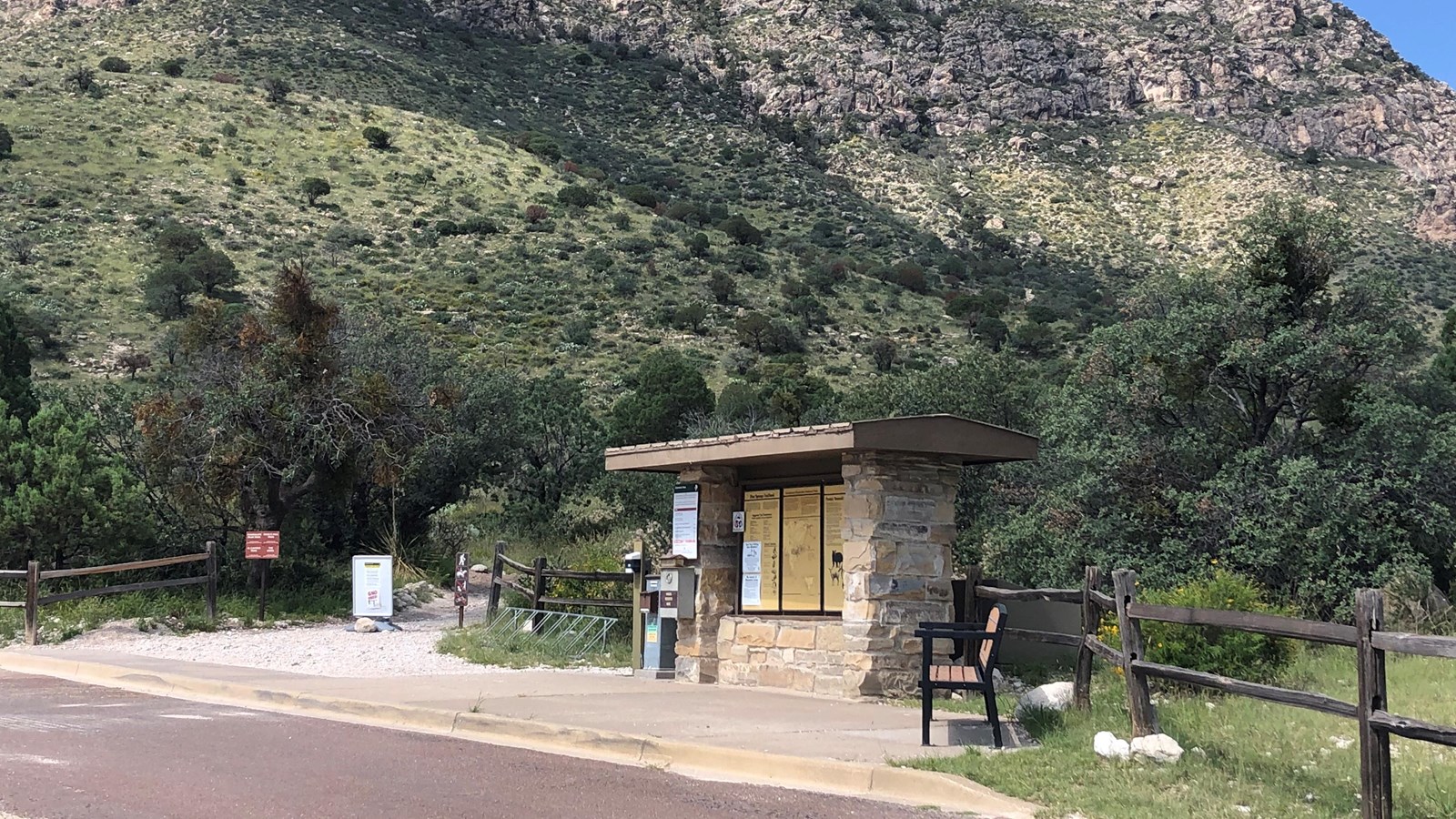 A stone kiosk with trail information marks the beginning of a trail in a desert mountain landscape. 
