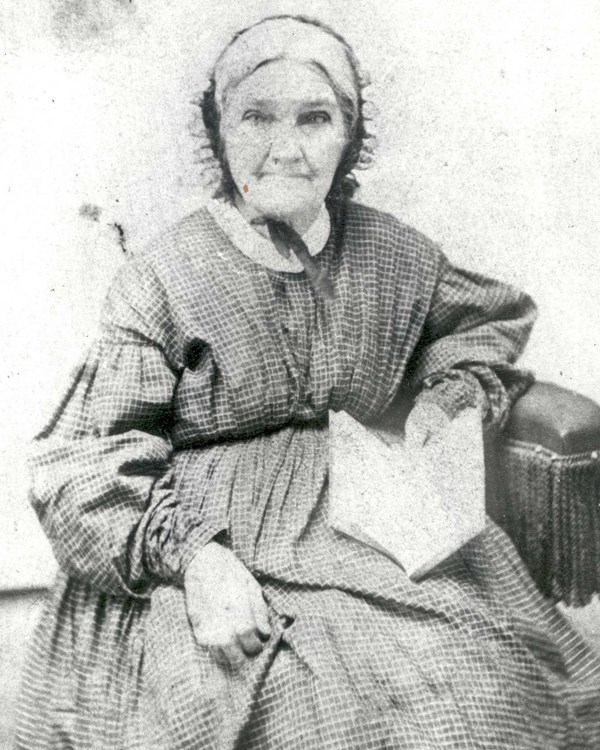 A black and white photograph of an elderly lady sitting in a fancy dress. She has a kind smile.