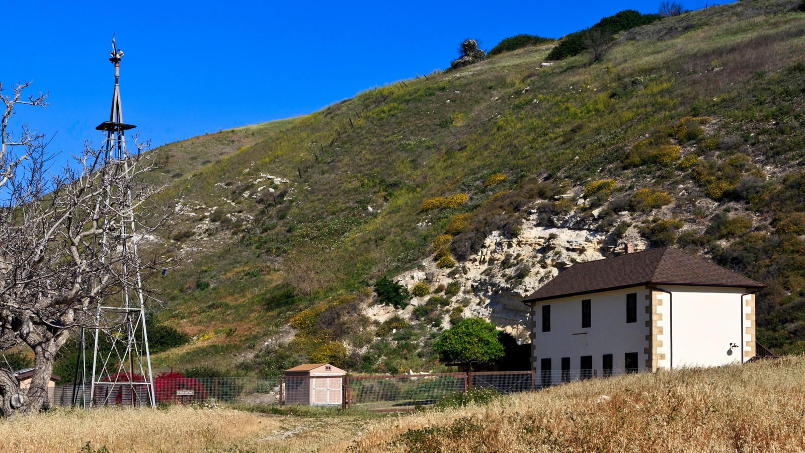 Windmill next to two story stone ranch house. 