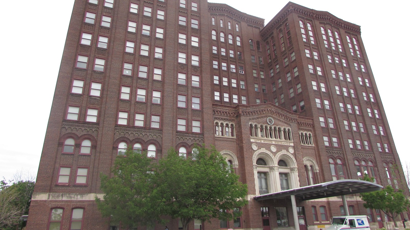 Large brick H-shape building. Center, recessed entry flanked by two large halves of building.