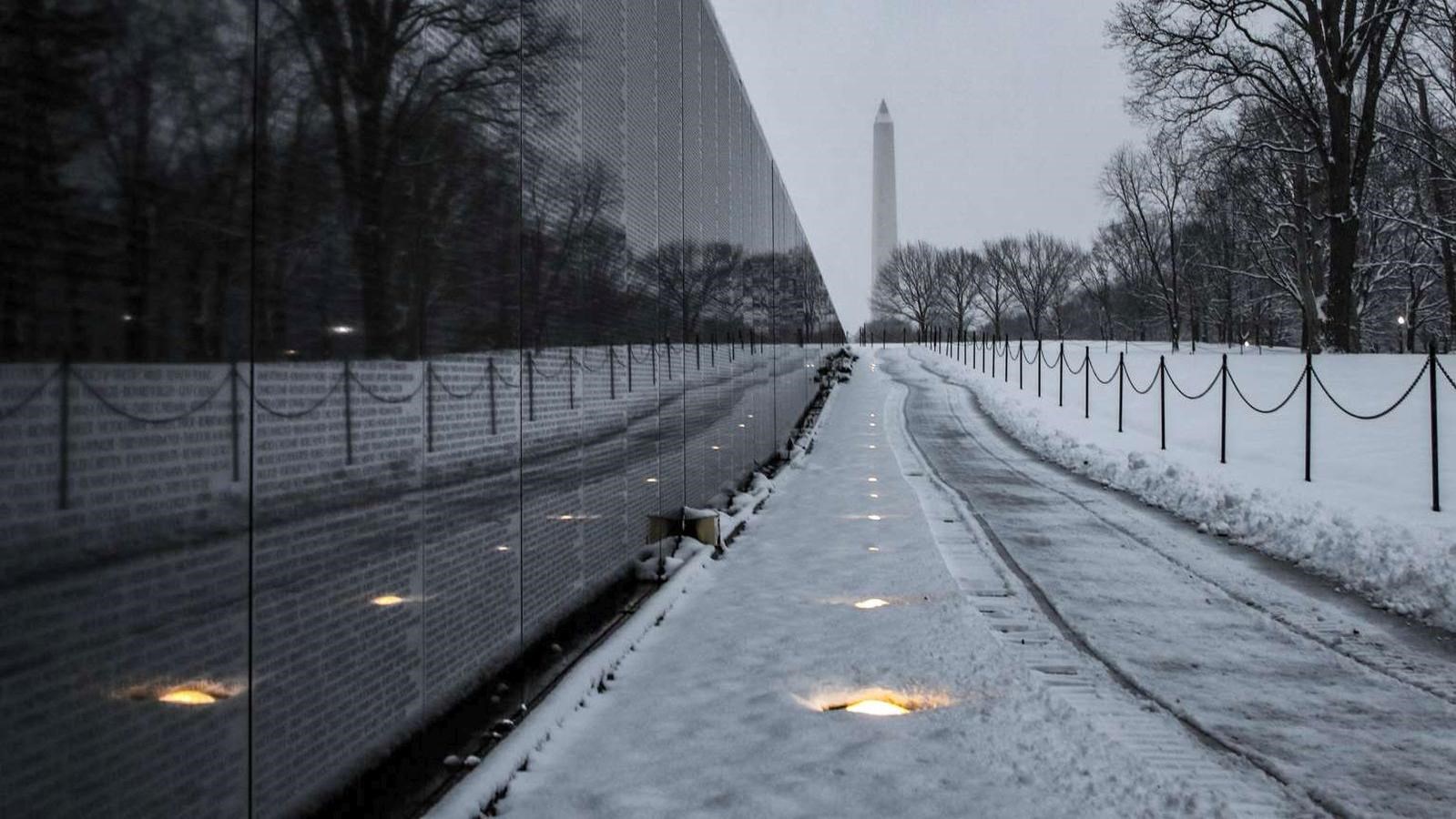 Snow-covered sidewalk and wall of Vietnam War Memorial wall leading towards the Washington Monument.