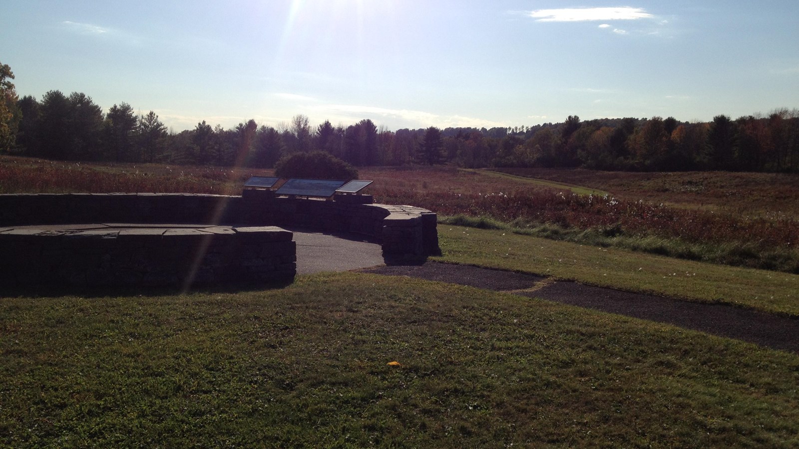 A stone walled overlook with an informational wayside overlooking a field.