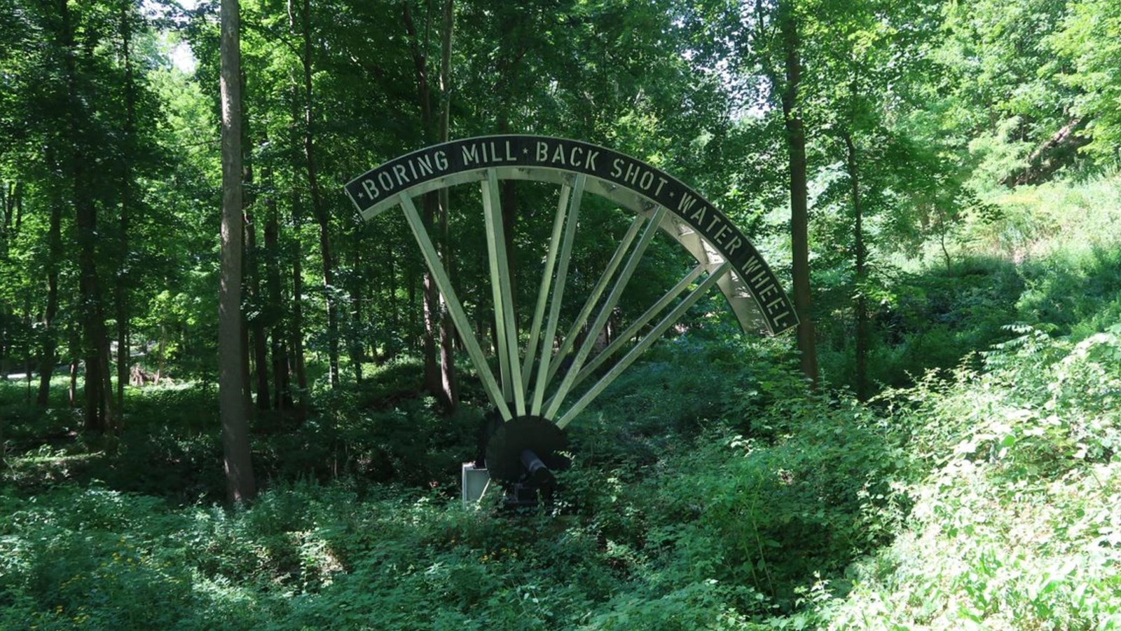 Green foliage surrounding signage on a steel recreation of a water wheel