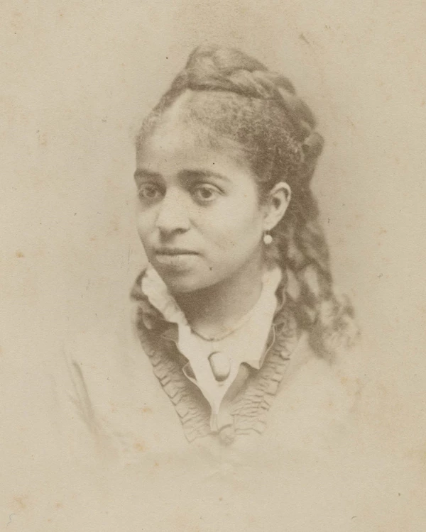 A young Black woman poses for a portrait with her hair half up in braids and a frilly dress.