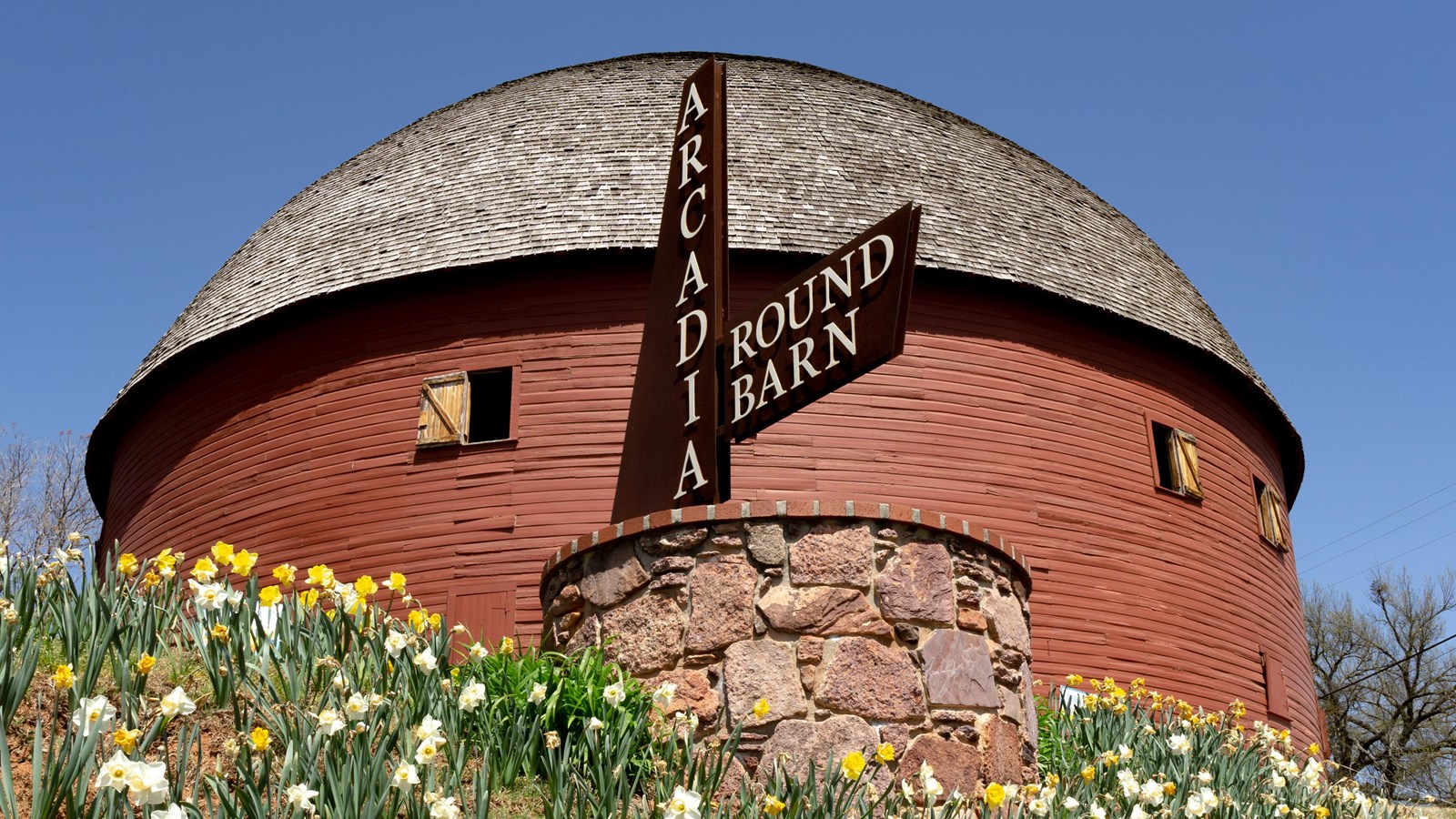 A red round shaped barn with a domed roof with shingles and a sign that reads