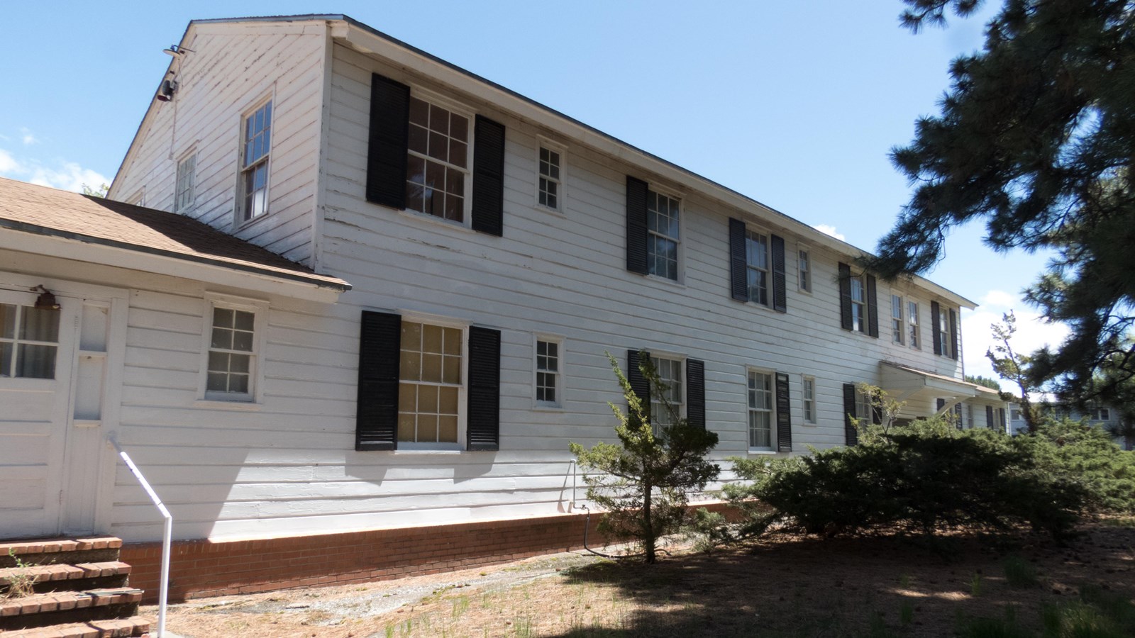 A long, two story white wood-sided building sits on a grass lawn