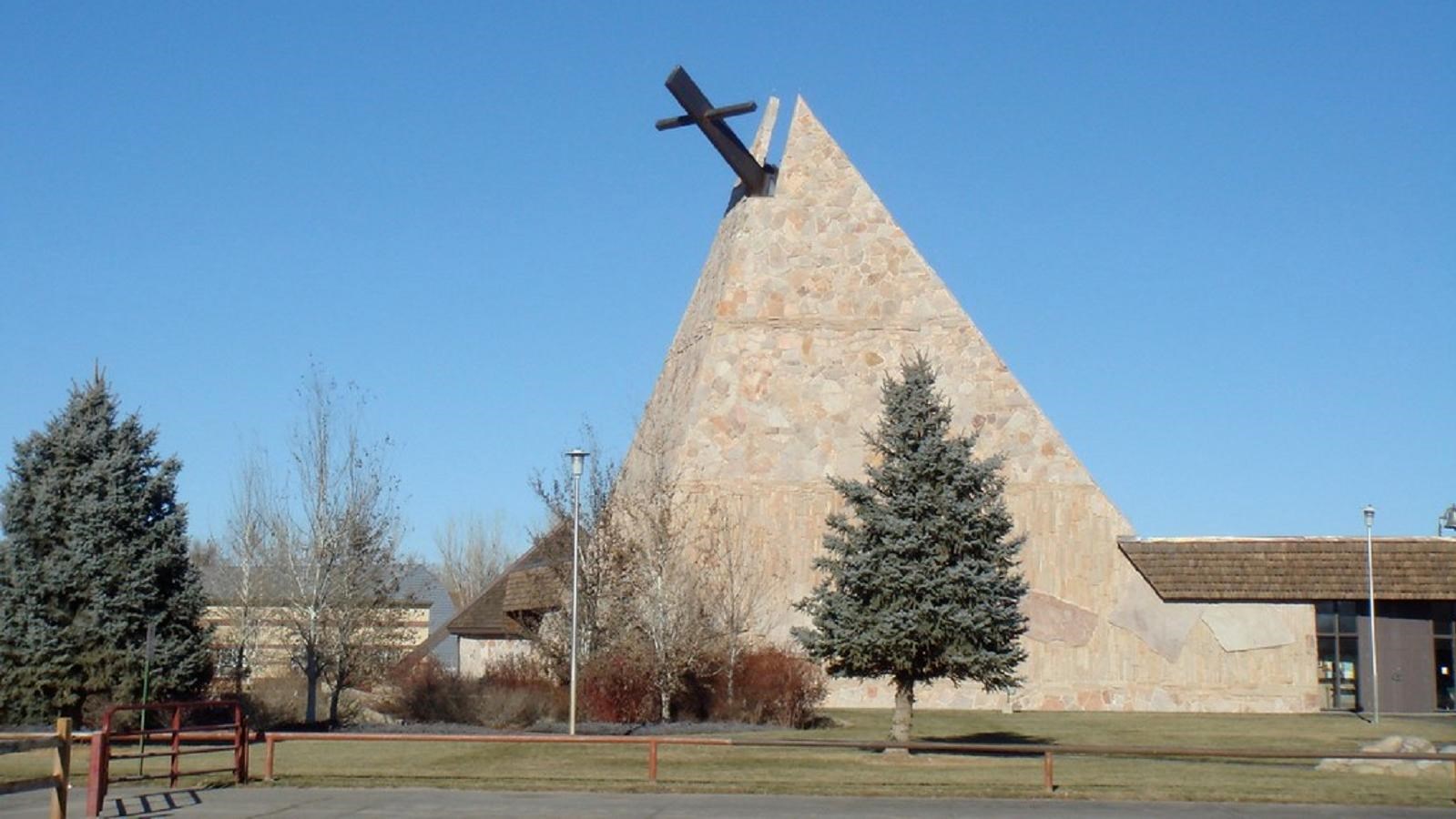 A tan stone teepee shaped structure with a brown cross protruding from its top.