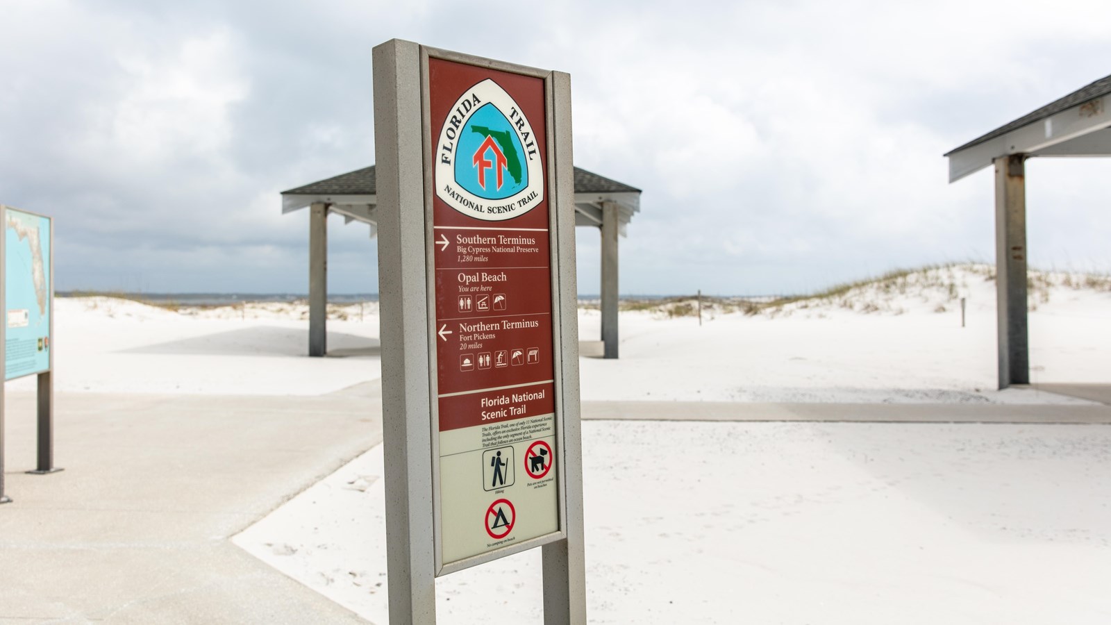 A sign for the Florida National Scenic Trail stands in front of pavilions at the beach.