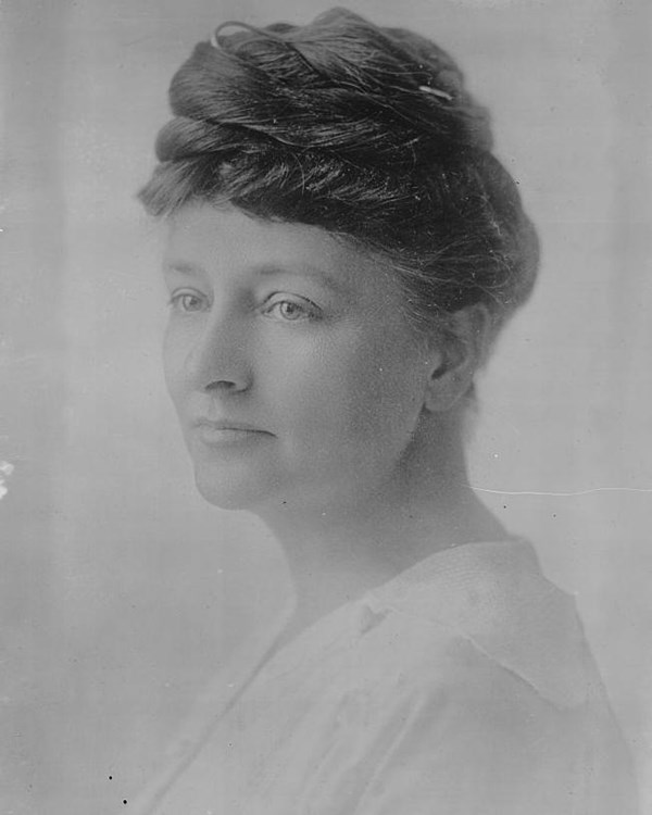 portrait of a woman with her hair braided up on top of her head. She wears a white blouse.
