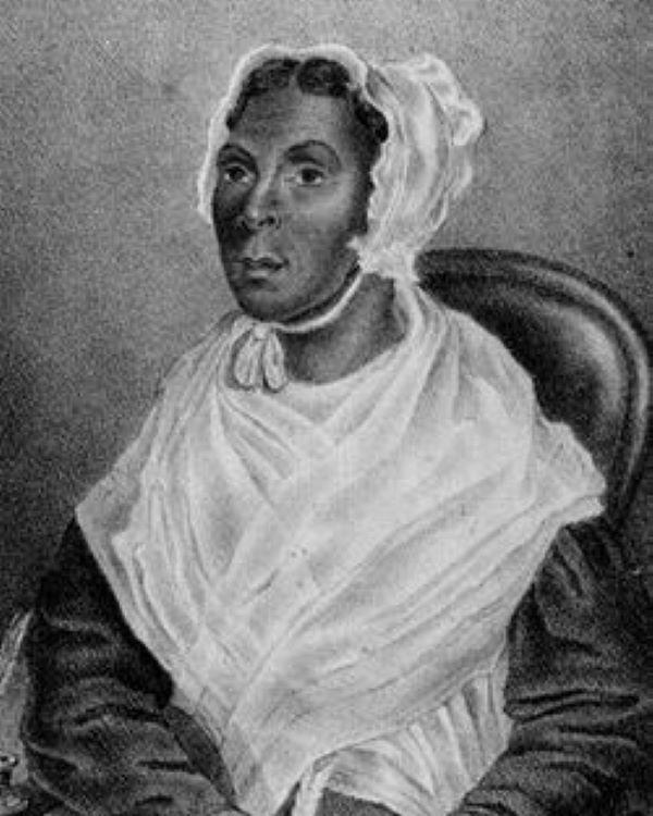 A woman with a white bonnet sitting in a chair.